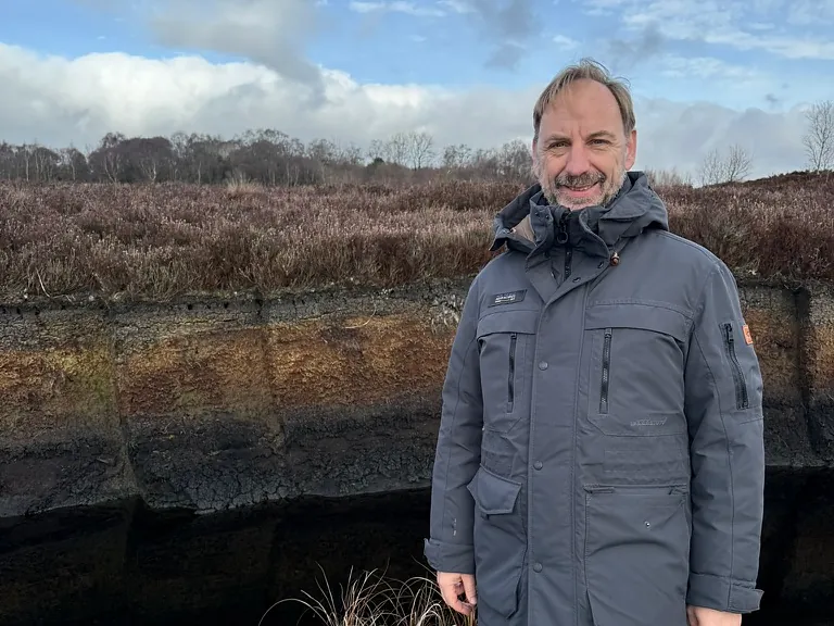 Bernhard Aumann vor einem offenen Torfprofil im Moor, davor Wasser